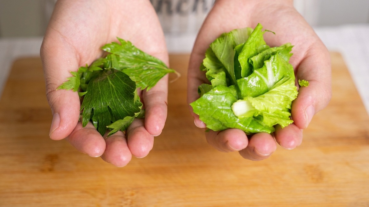 Dłonie trzymające posiekane liście selera i kapustę baby bok choy nad bambusową deską.