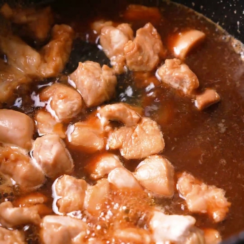 Kawałki kurczaka duszące się w bulgoczącym brązowym bulionie dashi na patelni.