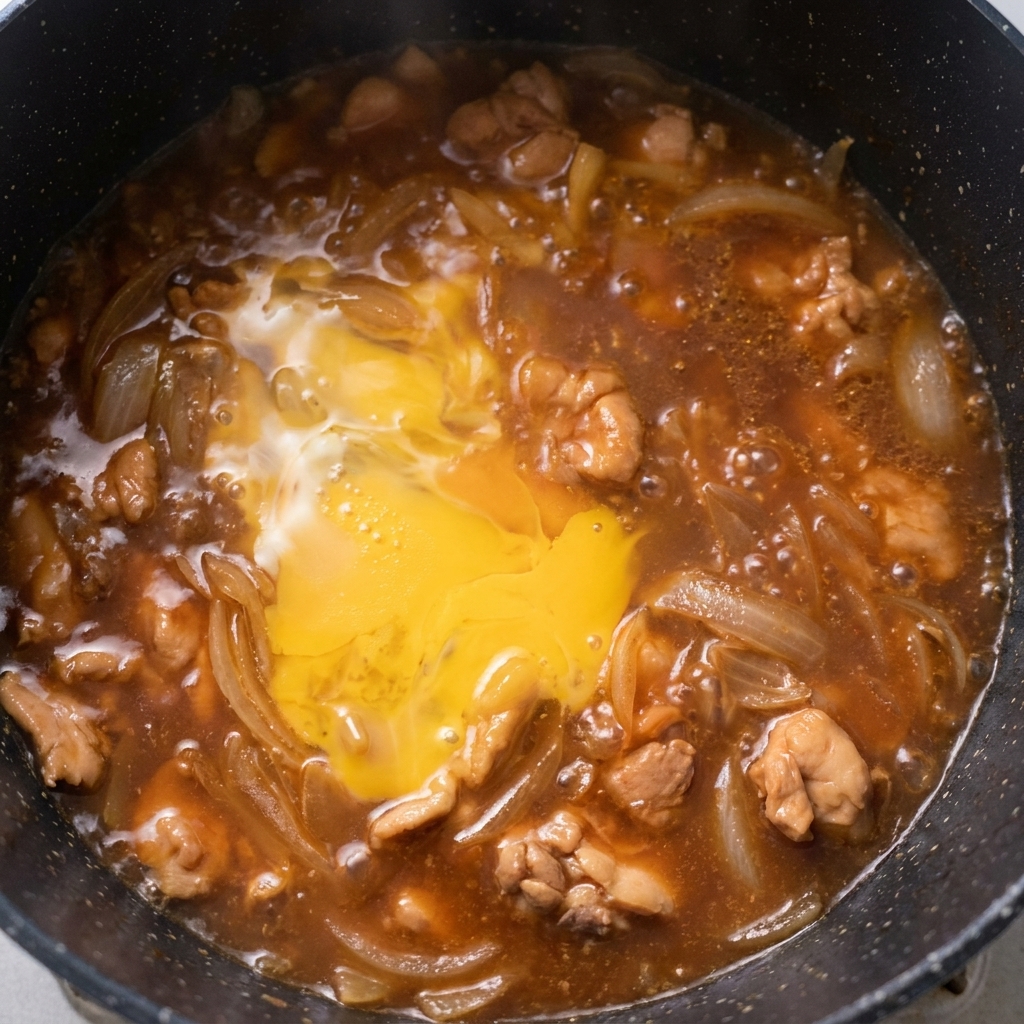 Częściowo ścięta warstwa jajek duszona z kurczakiem i cebulą na patelni.