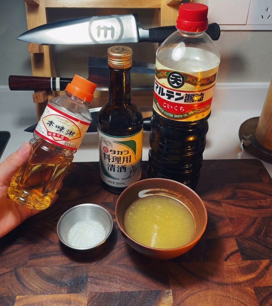Zestaw butelek mirin, sake i sosu sojowego obok miseczki z bulionem i cukrem.