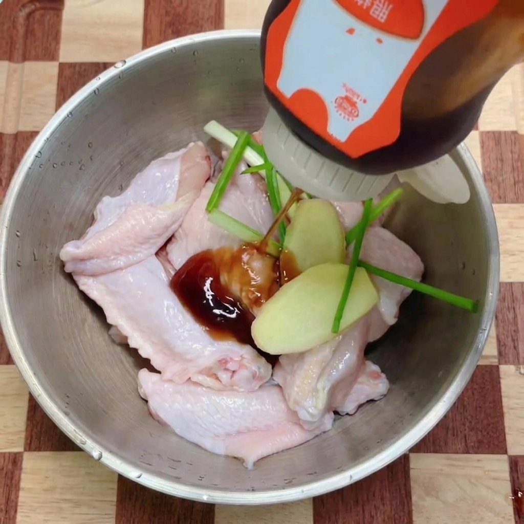 Ciemny sos teriyaki wylewany z butelki na miskę ze skrzydełkami kurczaka i świeżymi ziołami.