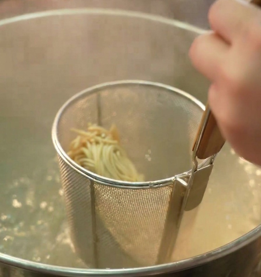 Sitko z makaronem ramen zanurzone w garnku z gotującą się wodą.