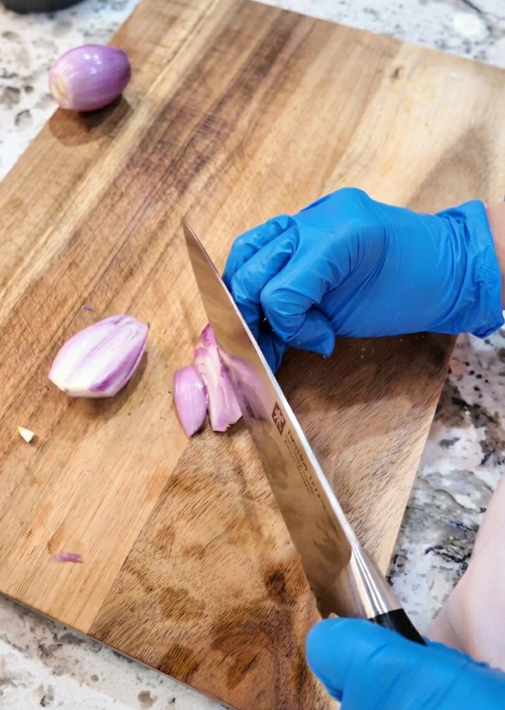 Nóż kuchenny krojący szalotki w cienkie plasterki na drewnianej desce.
