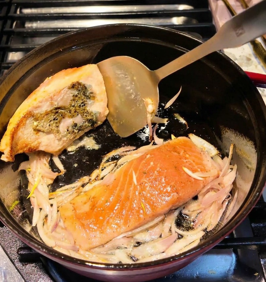 Metalowa łopatka obracająca filet z łososia w garnku, ukazująca złotobrązową powierzchnię.