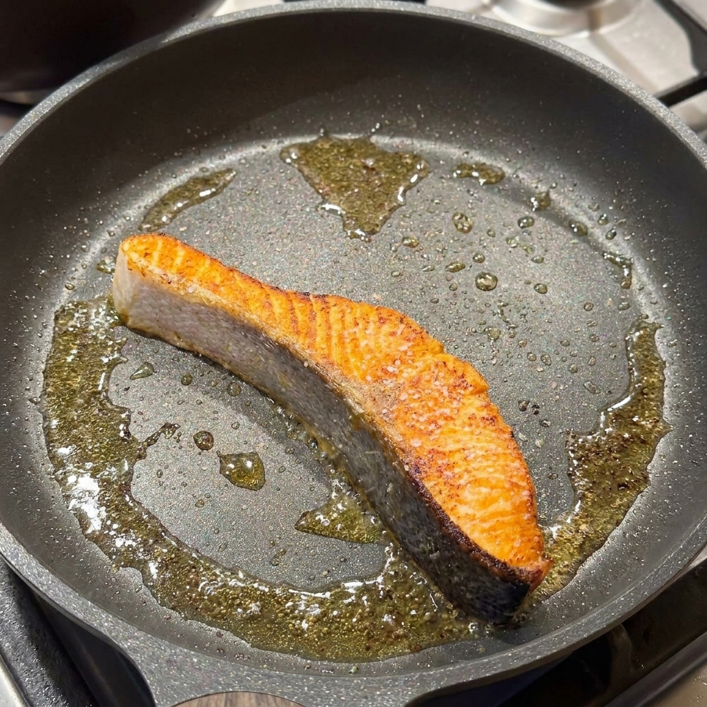 Podsmażony filet z łososia na patelni doprawiany solą i czarnym pieprzem.