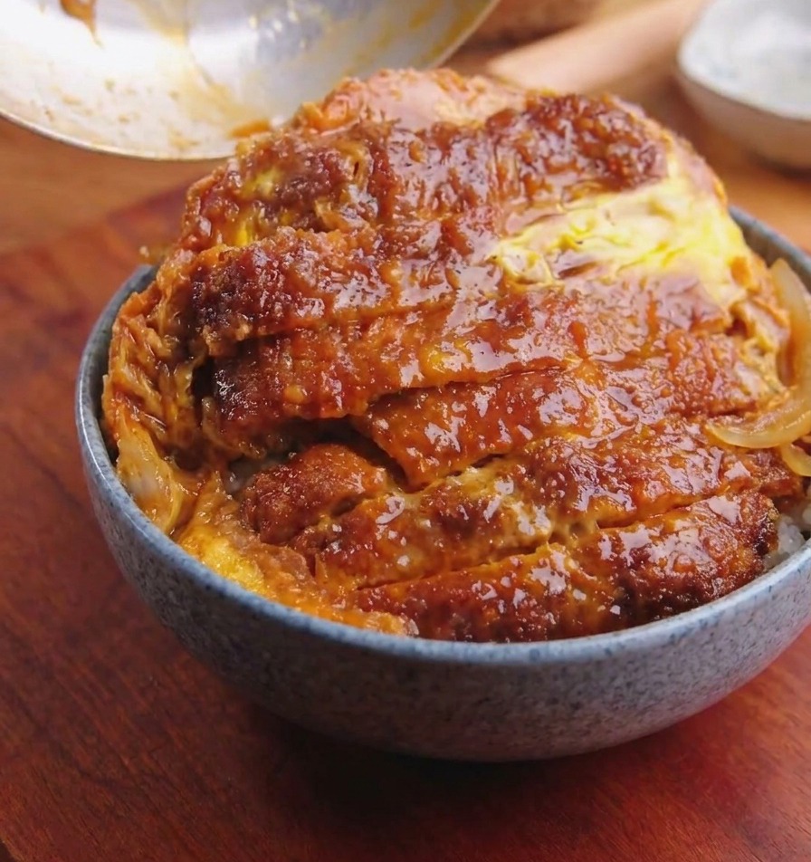 Patelnia przechylana nad miską, aby zsunąć kotlet z jajkiem i cebulą na ryż.