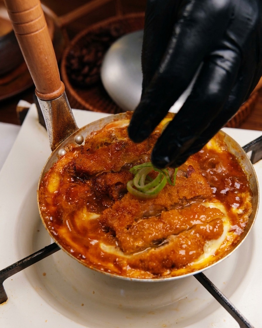 Dłoń posypująca gotowy Katsudon na patelni krążkami świeżej zielonej dymki.