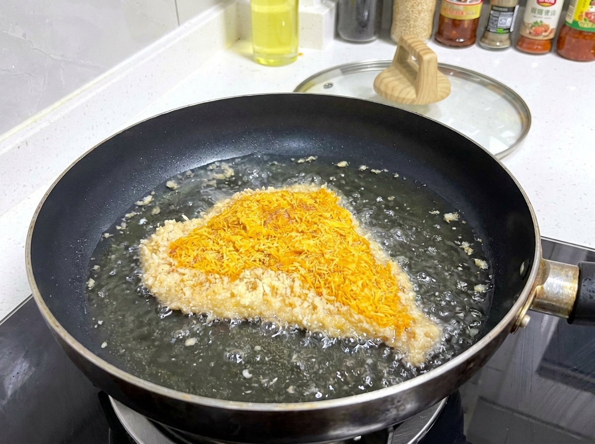 Spanierowany kotlet wieprzowy skwierczący na płytkiej patelni w gorącym oleju, z bąbelkami tworzącymi się wokół jego krawędzi.