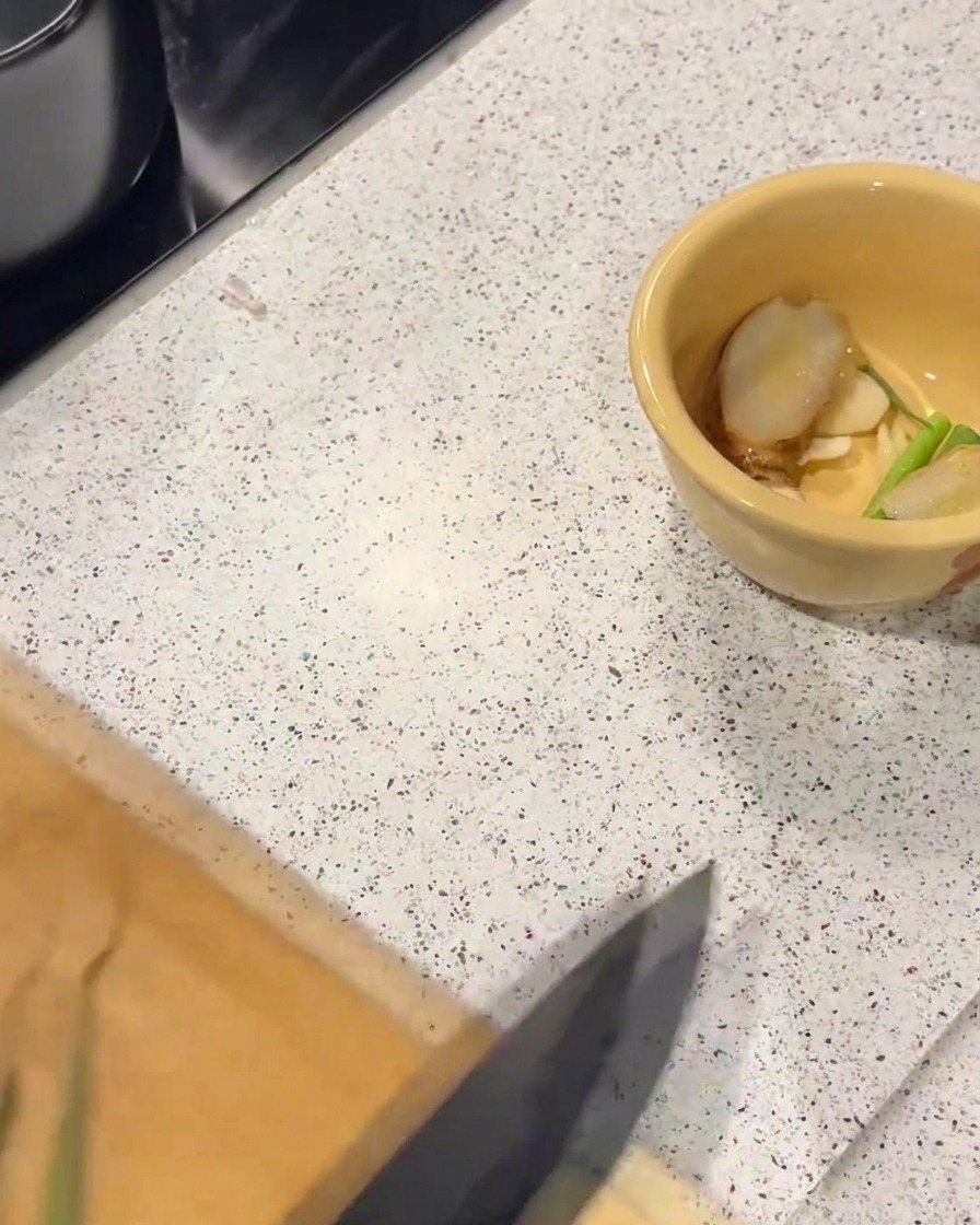 Żółta ceramiczna miseczka z plasterkami imbiru i kawałkami szczypiorku na blacie kuchennym.