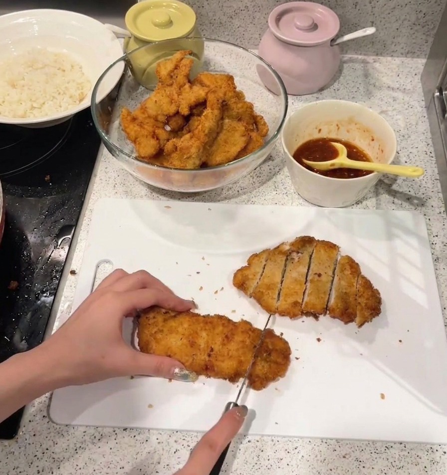 Osoba krojąca chrupiący, złocisty kotlet z kurczaka na paski na białej plastikowej desce do krojenia.