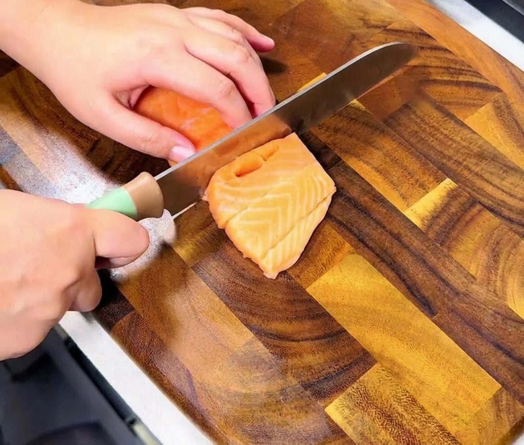 Dłonie krojące świeży pomarańczowy filet z łososia na równe, apetyczne kawałki w kształcie kostki.
