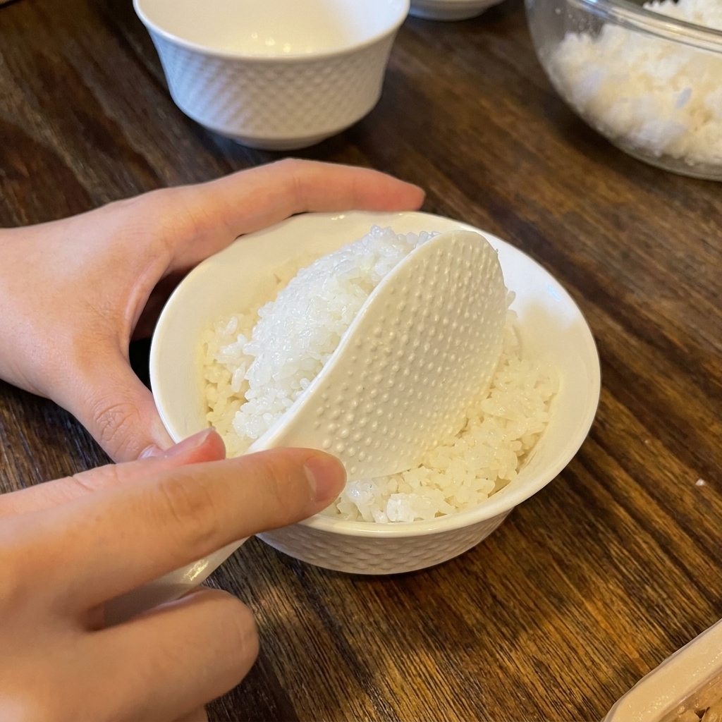 Biała łopatka nakładająca porcję doprawionego ryżu do małej białej ceramicznej miseczki o ciekawej teksturze.