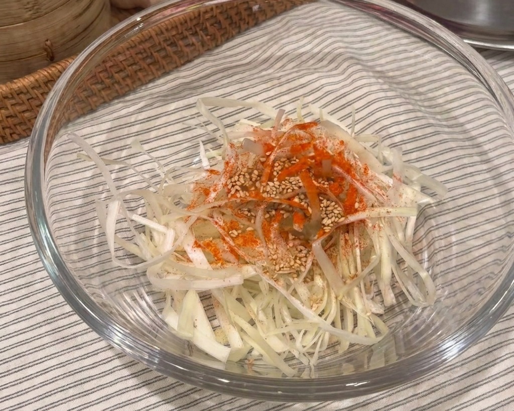 Szklana miska z pokrojoną dymką, posypana płatkami chili i białym sezamem.