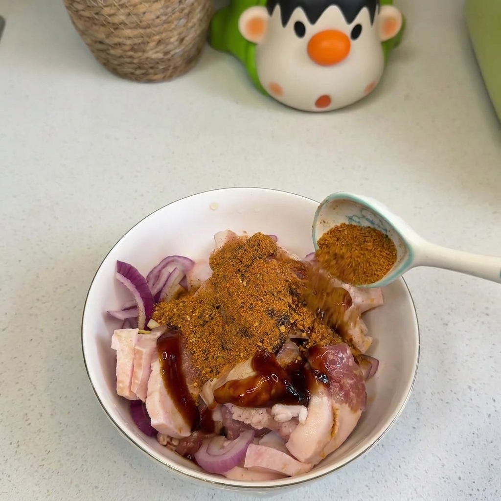 Dłoń sypiąca pomarańczową przyprawę BBQ i czerwone chili na surowy boczek z cebulą.