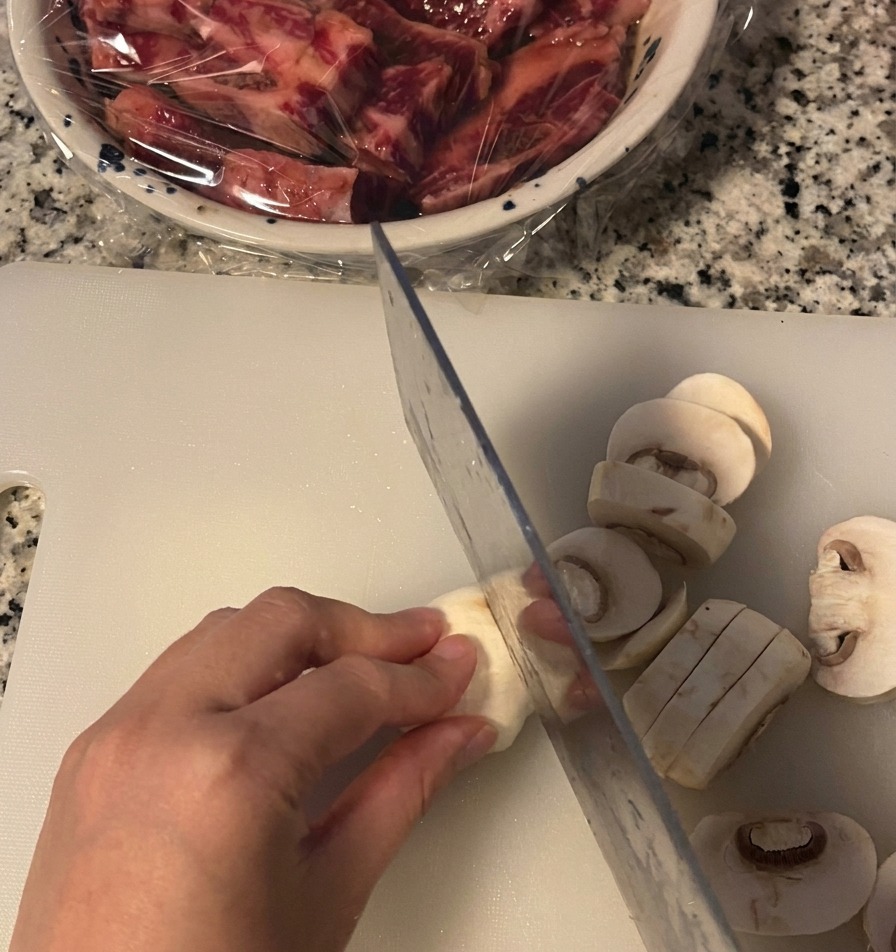 Ręka krojąca pieczarkę w grube plasterki na białej desce do krojenia.