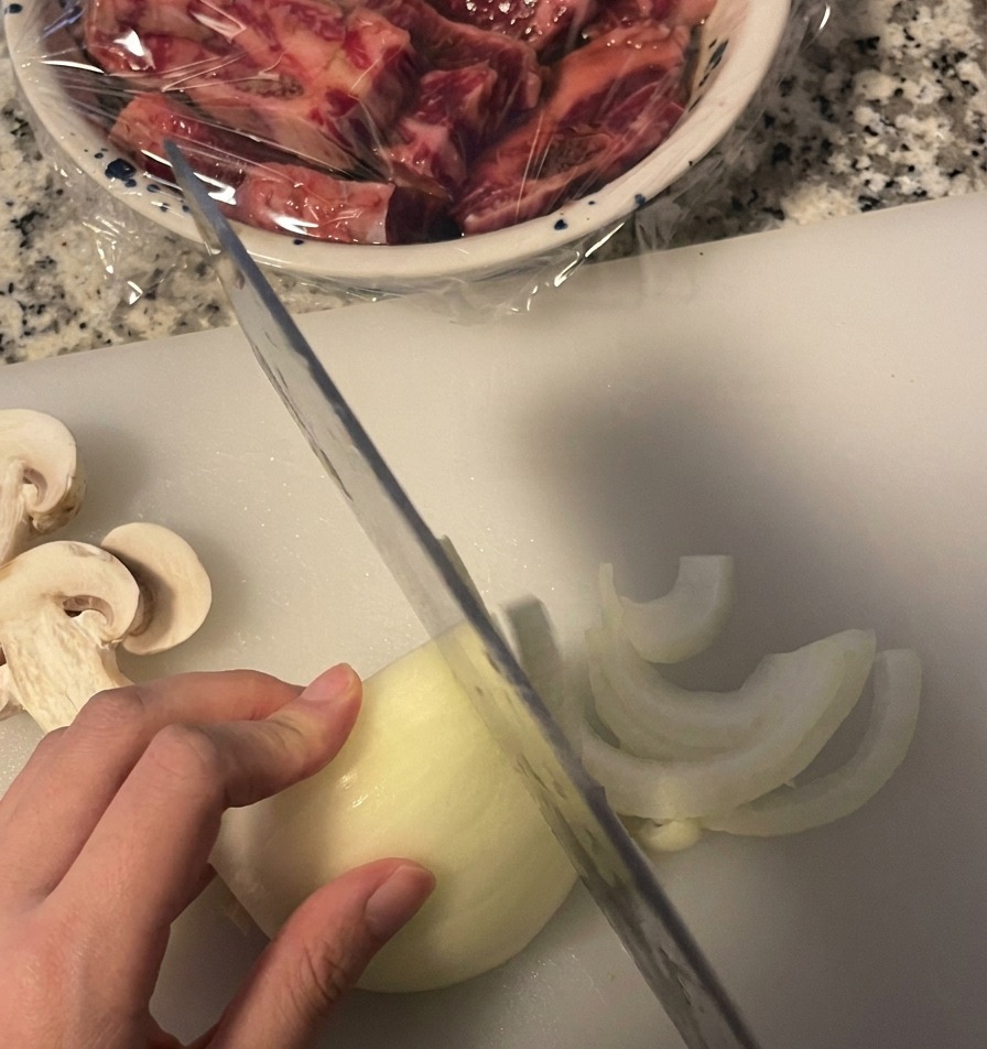 Cięcie białej cebuli w cienkie piórka na białej desce do krojenia przy użyciu noża kuchennego.