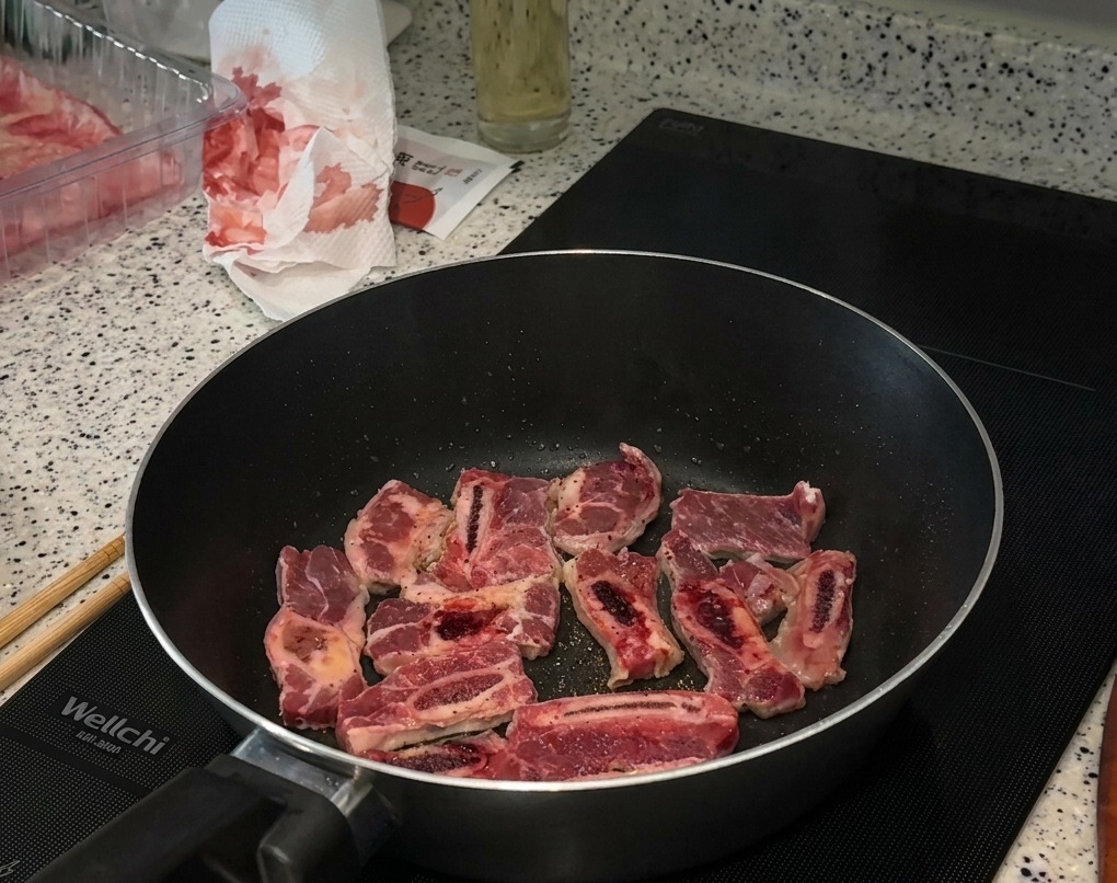 Smażące się żeberka wołowe na patelni indukcyjnej, posypane solą i pieprzem.