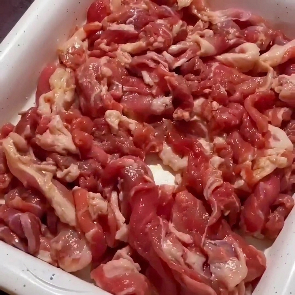 Zbliżenie na wieprzowinę smażoną na patelni, której brzegi stają się brązowe i chrupiące.