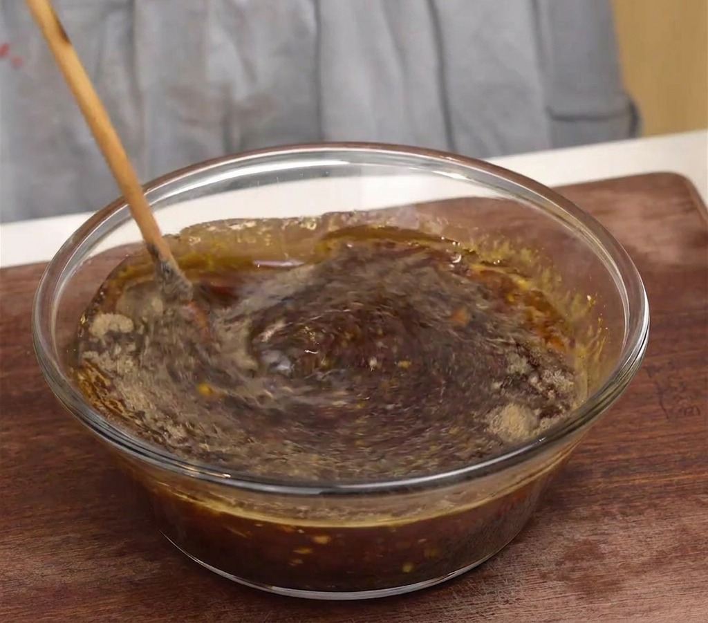 Drewniana łyżka mieszająca ciemną, aromatyczną koreańską marynatę w szklanej misce.