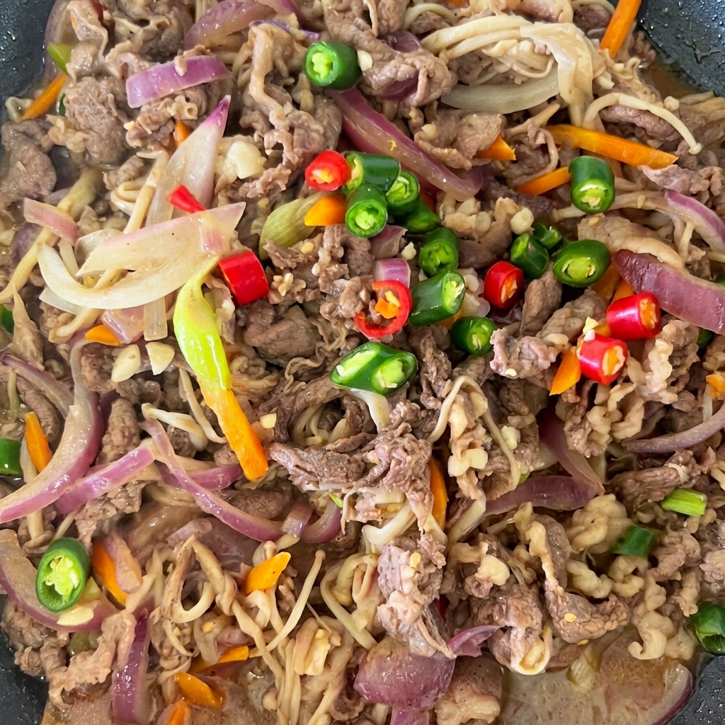 Kolorowe plasterki czerwonego i zielonego chili ułożone na wierzchu gotowego bulgogi na patelni.