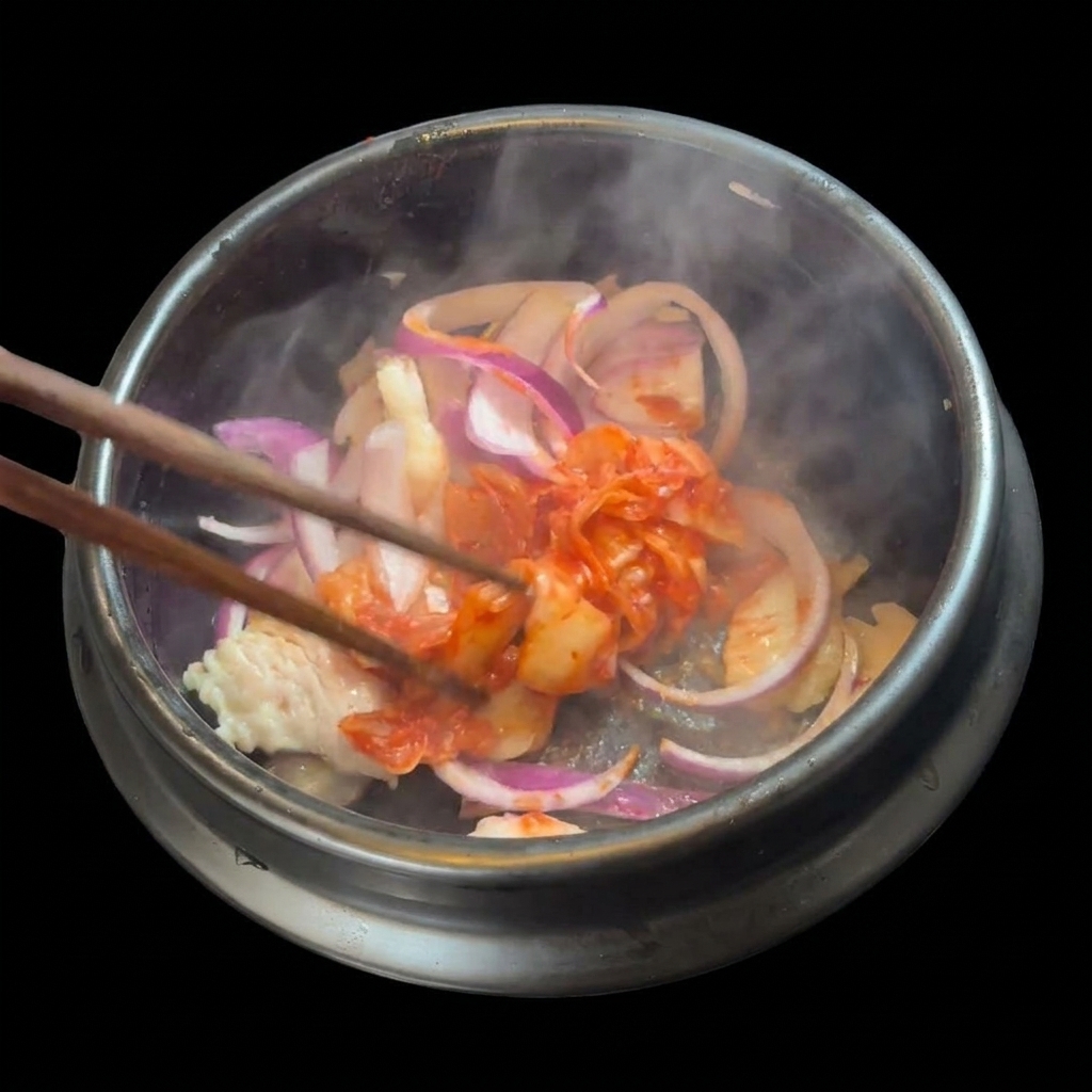 Garść posiekanego czerwonego kimchi dodawana do podsmażonego boczku i cebuli.