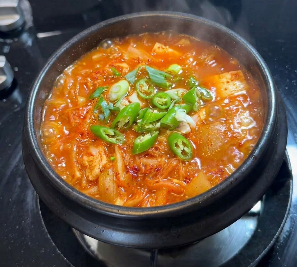 Plastry zielonego chili i dymki rozrzucone na powierzchni bulgoczącego gulaszu kimchi.
