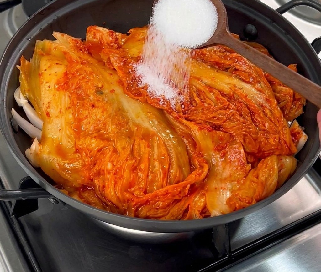 Biały cukier sypany z drewnianej łyżki na warstwę czerwonego kimchi.