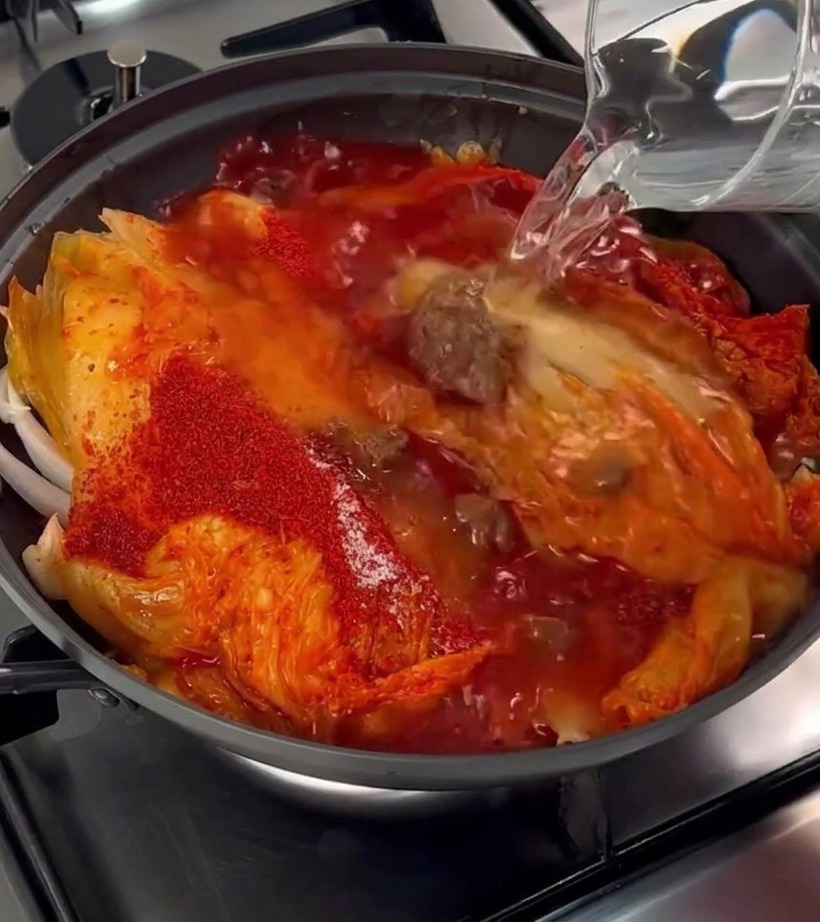 Czysta woda wlewana ze szklanego dzbanka do naczynia z kimchi i boczkiem.