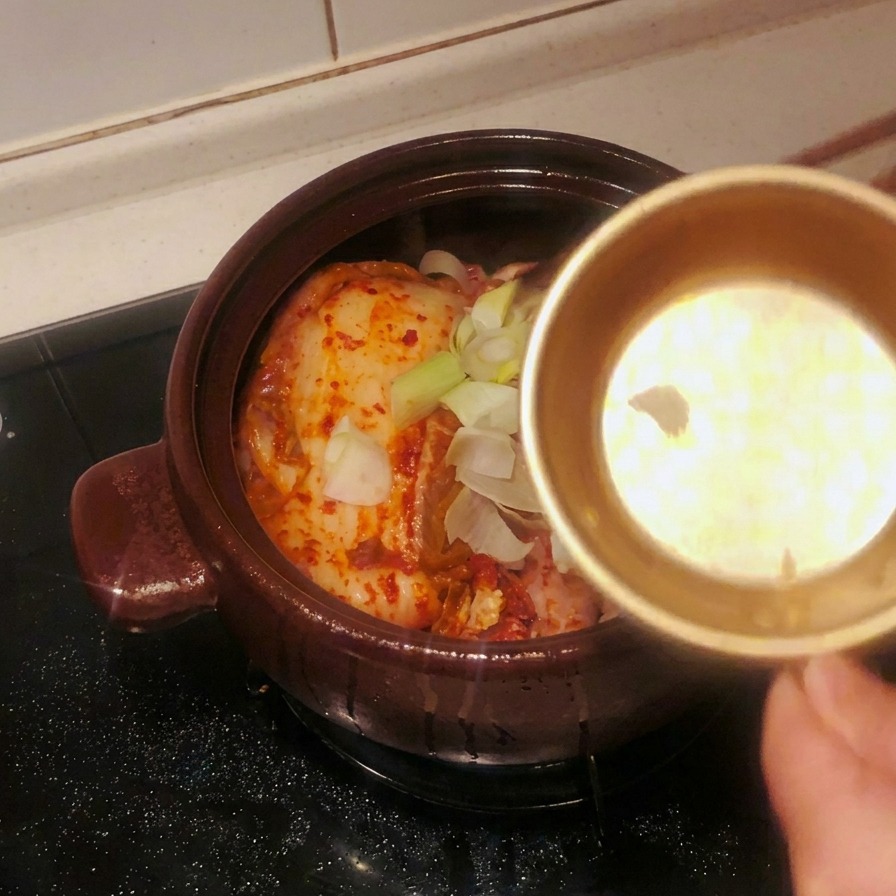 Metalowa miseczka, z której wsypywany jest posiekany czosnek i kawałki dymki na kimchi w naczyniu.
