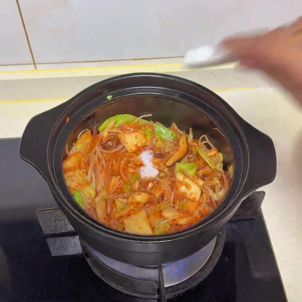 Szczypta białej soli dodawana do garnka z warzywami i kimchi.
