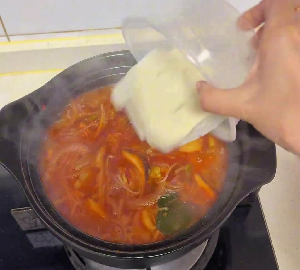 Świeże białe kostki tofu przekładane z przezroczystego pojemnika do gotującej się zupy kimchi.