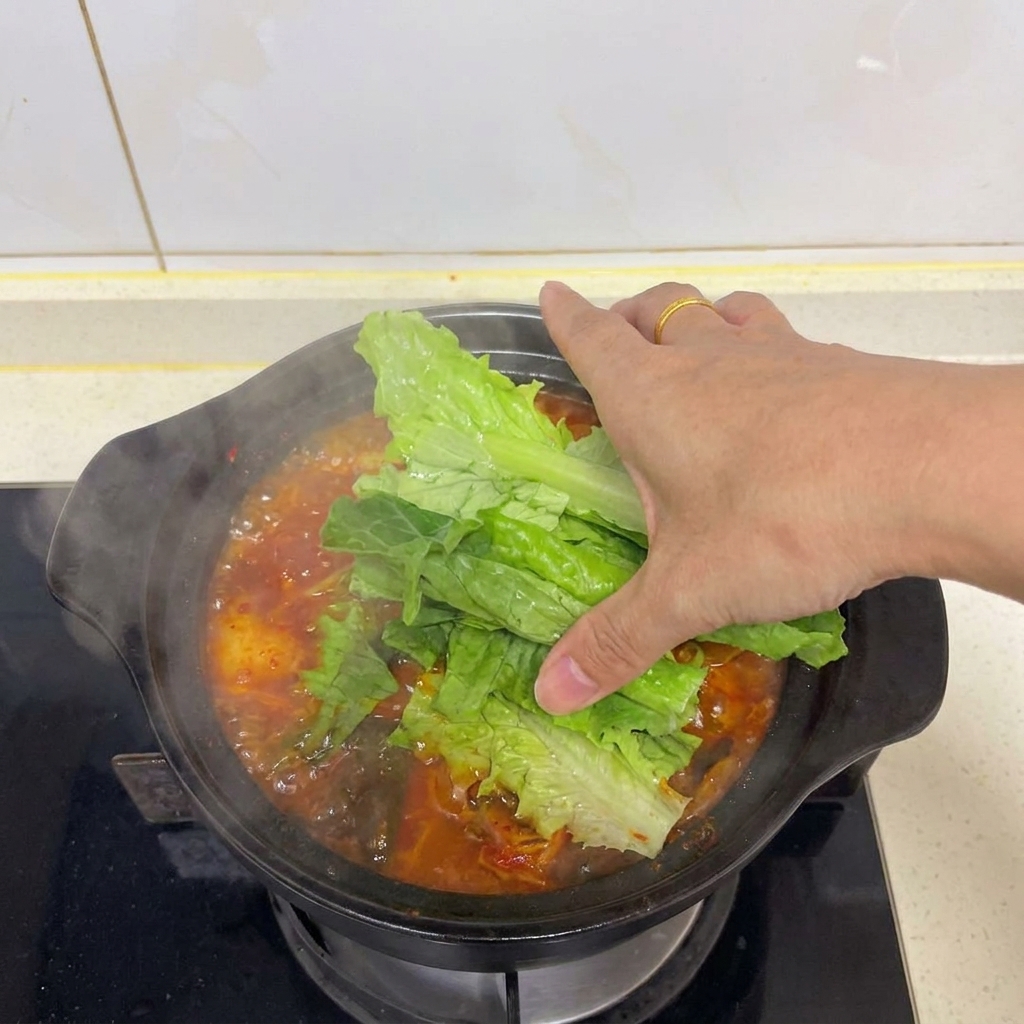 Dłoń układająca świeże liście sałaty na wierzchu parującej zupy kimchi z tofu.