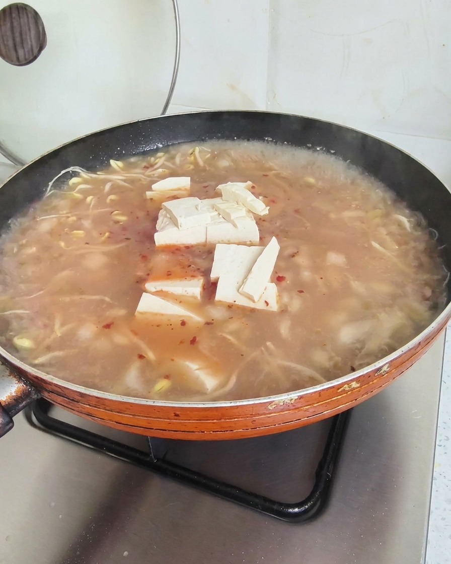 Kostki tofu unoszące się na powierzchni czerwonawej zupy w dużej patelni.