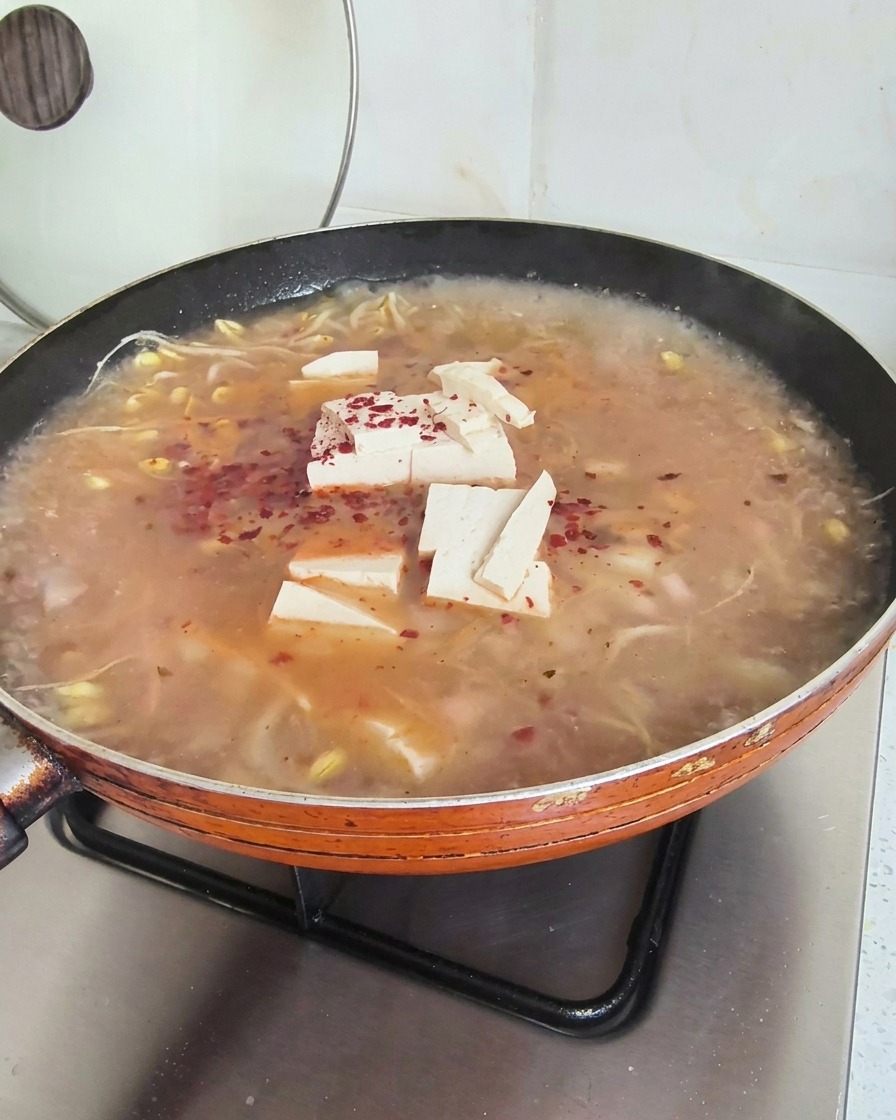 Intensywnie czerwone płatki chili posypane na wierzchu gotującej się zupy z tofu i kiełkami.