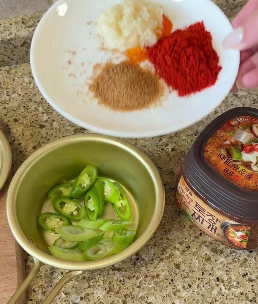 Dłoń trzymająca talerz z czosnkiem i przyprawami obok pokrojonego chili i słoika z pastą sojową.