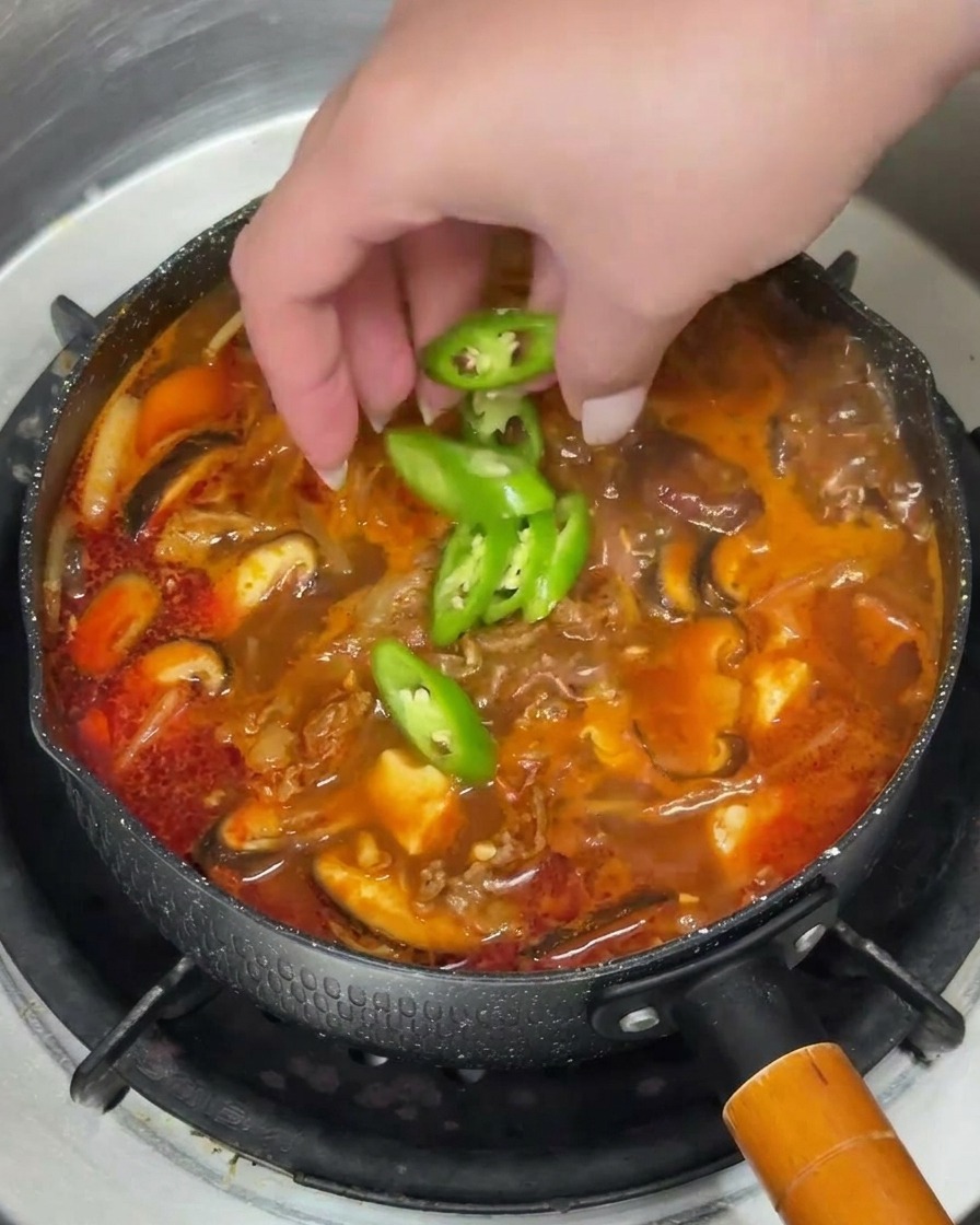 Posypywanie czerwonej zupy kawałkami zielonego chili i posiekaną dymką.
