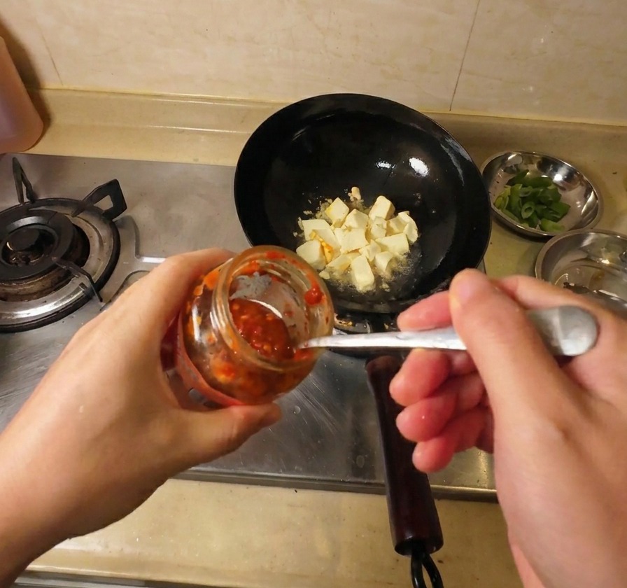 Zbliżenie na dodawanie czerwonego sosu chili z słoiczka do woka ze złocistym tofu.