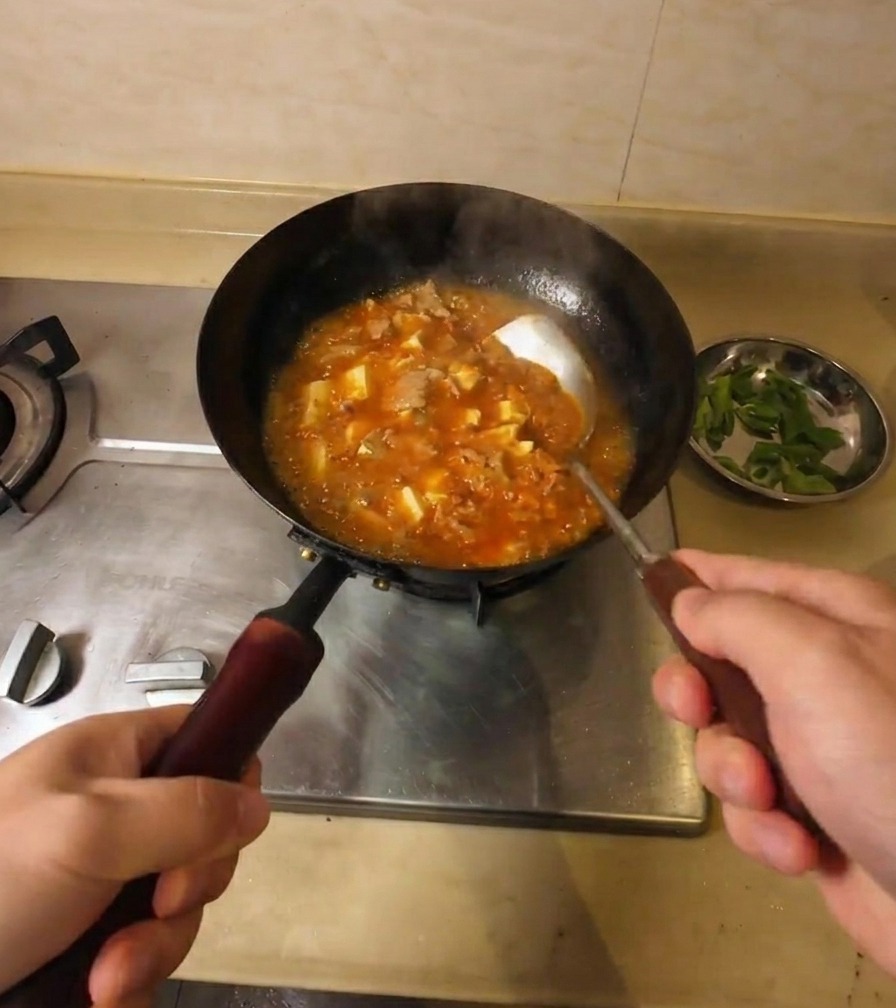 Mieszanie gęstniejącej, pomarańczowo-czerwonej zupy z tofu i wołowiną na kuchence.