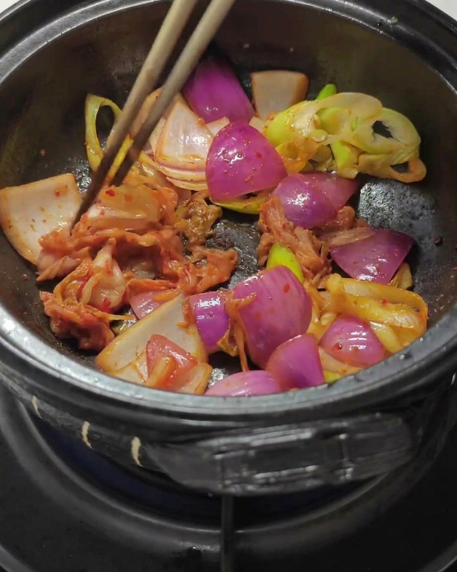 Pałeczki mieszające posiekane kimchi i pastę paprykową z podsmażoną cebulą w garnku.