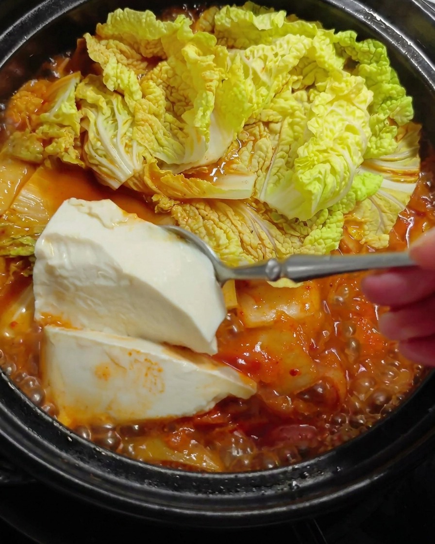 Duża łyżka delikatnie nakładająca białe tofu do gorącego, czerwonego gulaszu.