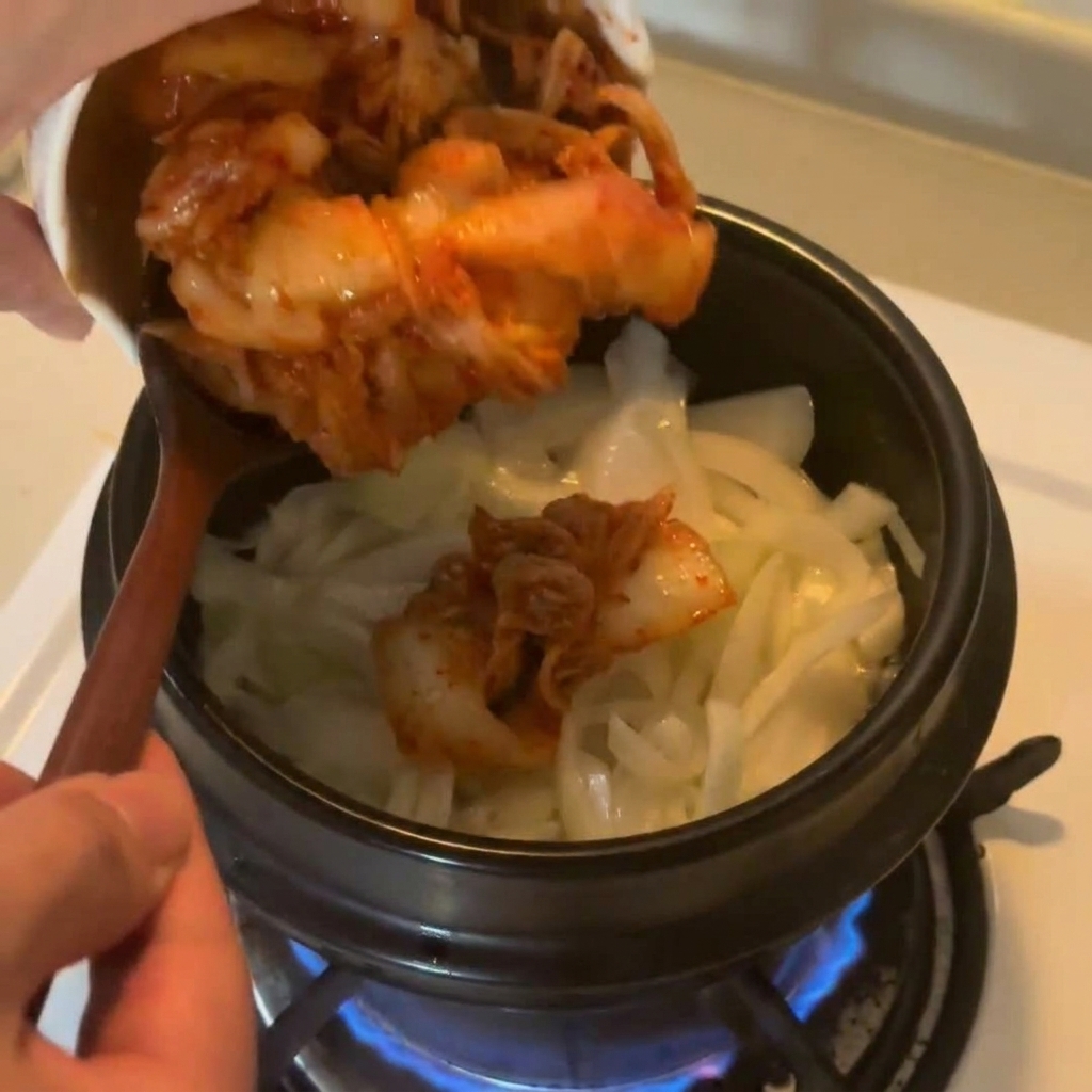 Posiekane kimchi przekładane z miseczki do garnka z podsmażoną cebulą.