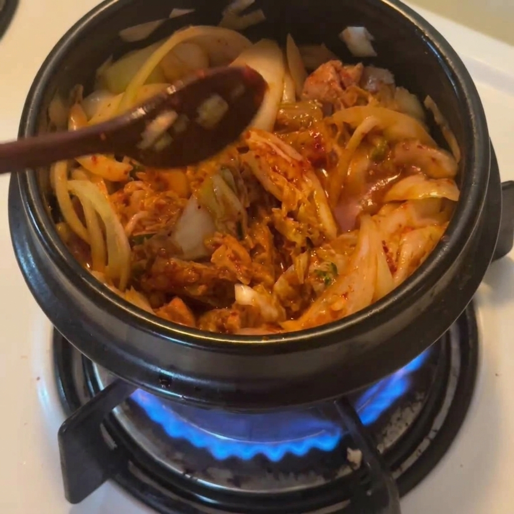 Sypanie czerwonej koreańskiej papryki gochugaru do garnka z tuńczykiem i kimchi.