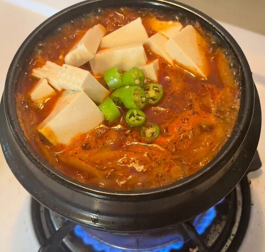 Gotowy gulasz z kimchi w czarnym garnku, udekorowany tofu i świeżym zielonym chili.
