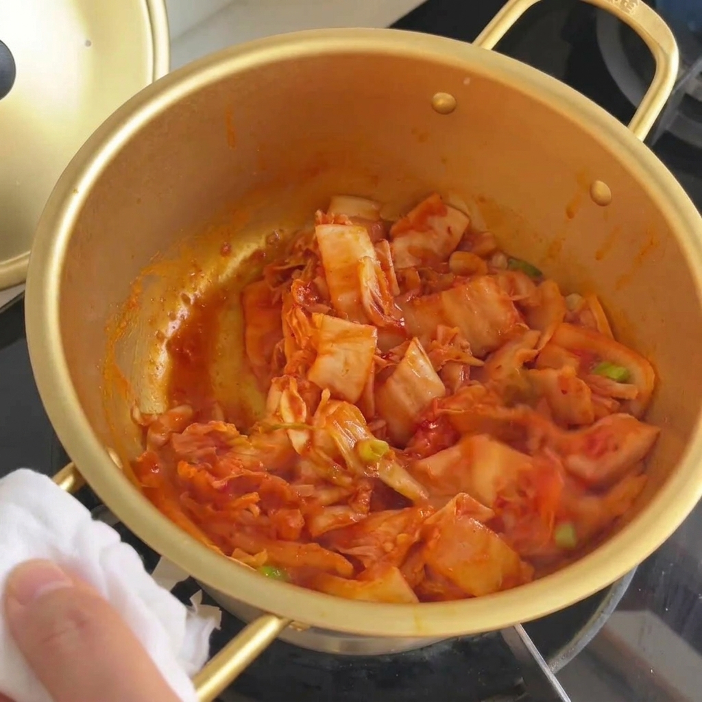 Mieszanie kimchi z dymką w garnku, aż kapusta stanie się lekko szklista.