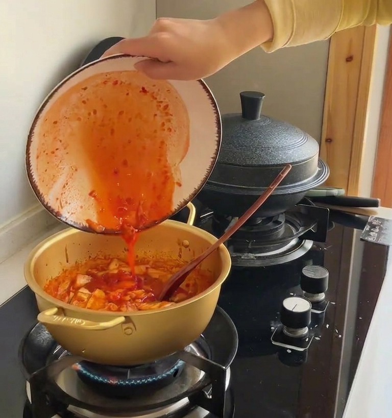 Intensywnie czerwony sok z kimchi wlewany z ceramicznej miseczki do garnka.