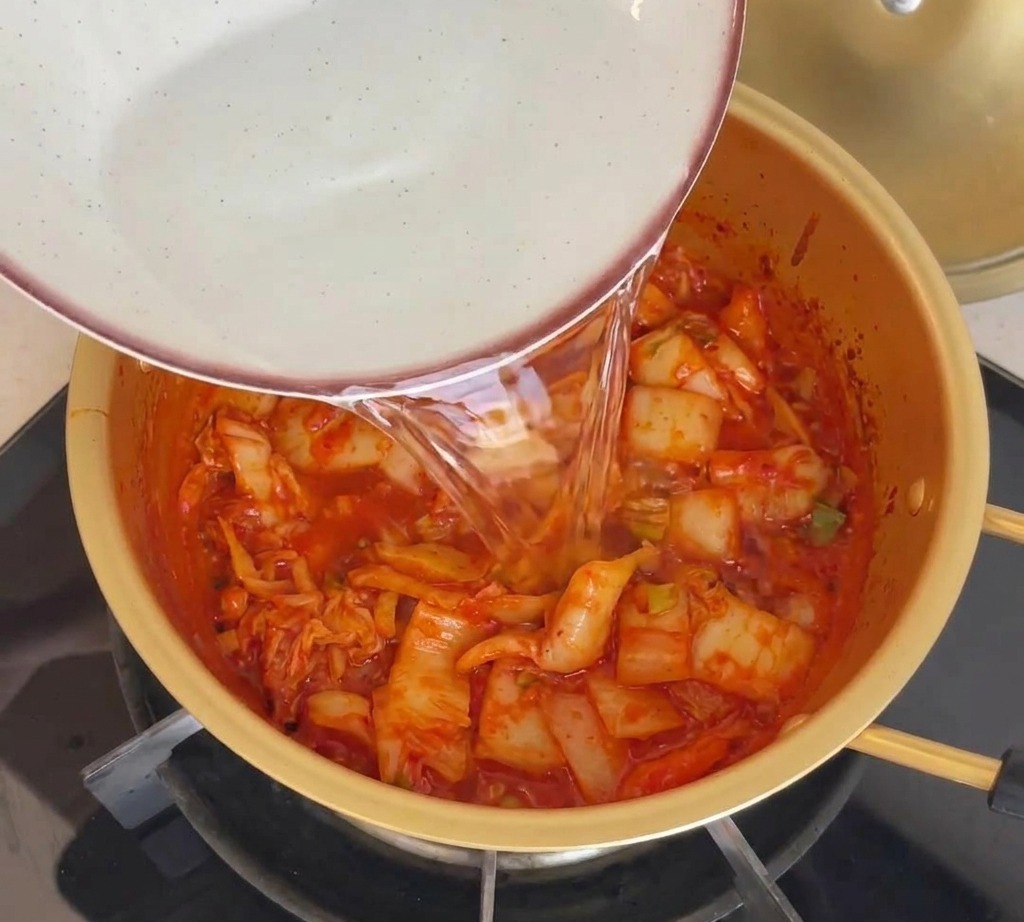 Woda wlewana z miski do garnka z podsmażonym czerwonym kimchi.