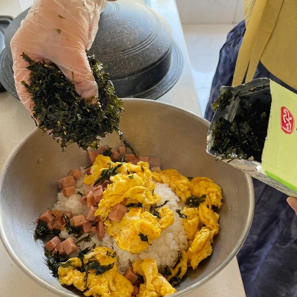 Duże kawałki tuńczyka z puszki dodawane do gotującego się, czerwonego gulaszu kimchi.