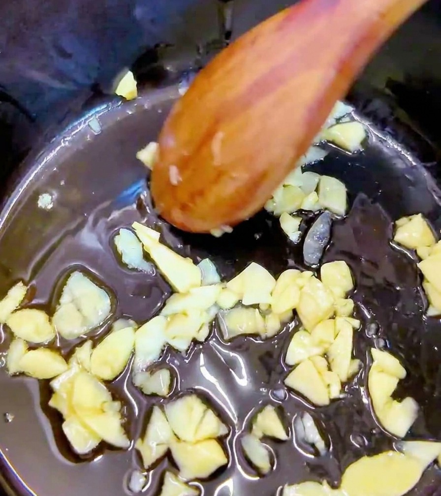 Kawałki ostrego, czerwonego kimchi mieszane z czosnkiem w garnku za pomocą drewnianej łyżki.