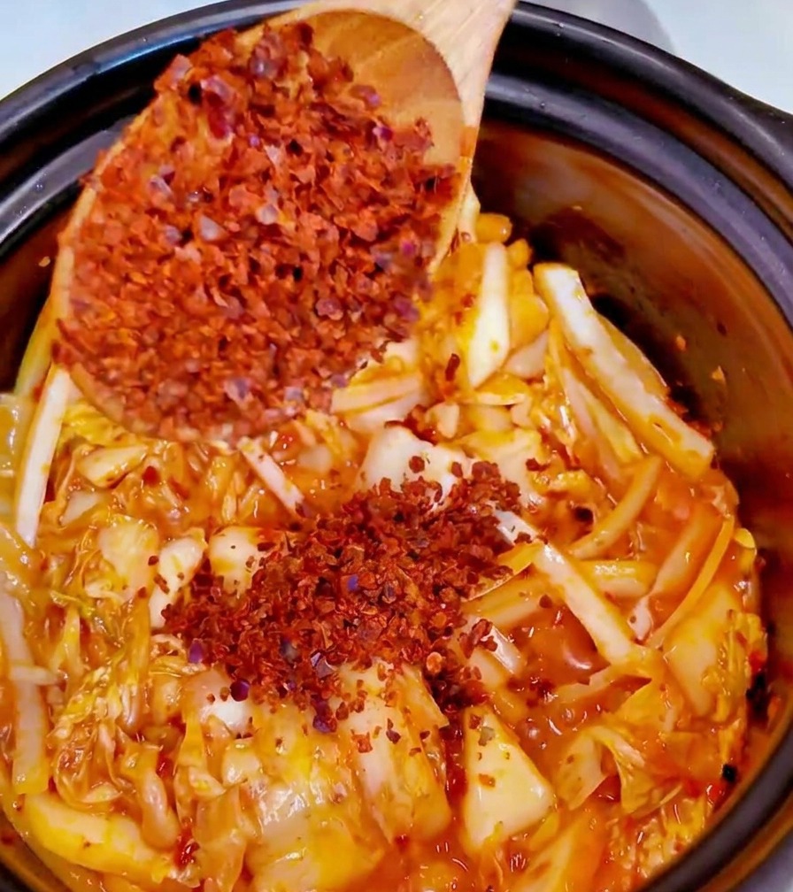 Wsypywanie drobnego proszku chili do garnka z kimchi i aromatycznymi warzywami.