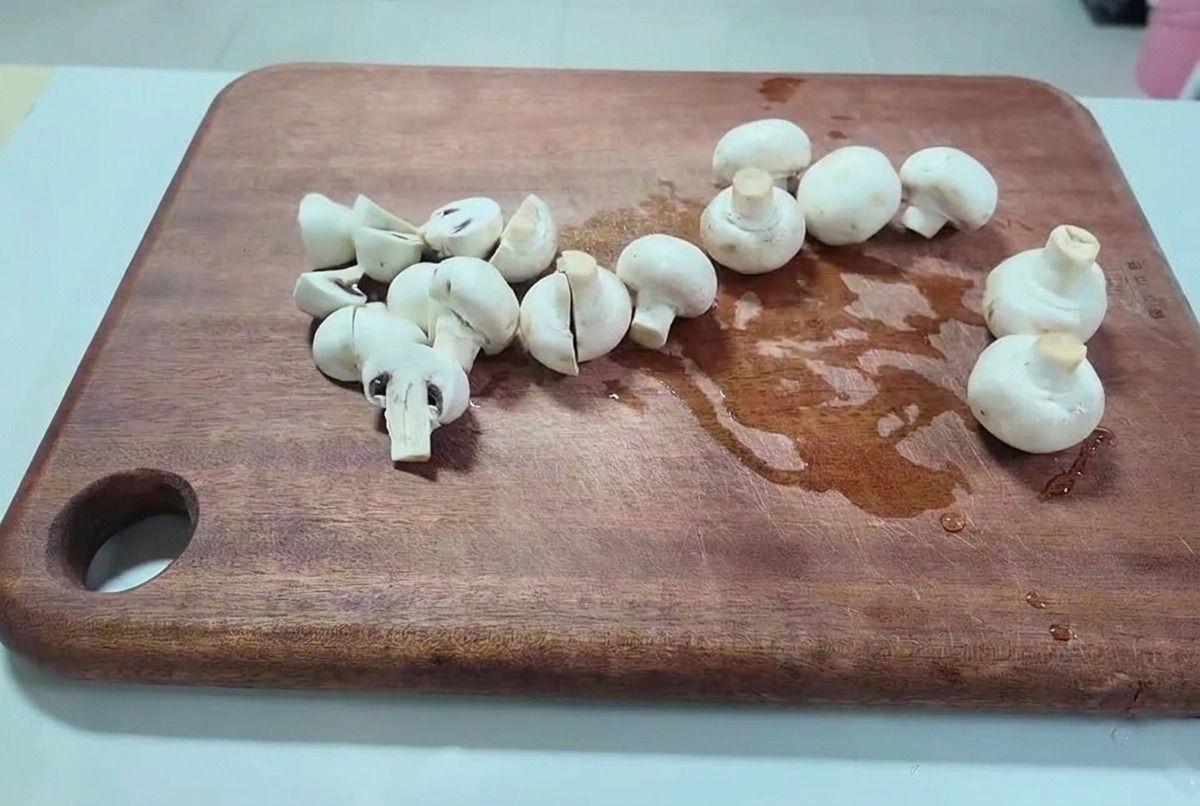 Świeże białe pieczarki krojone na połówki i grubsze plastry na ciemnej drewnianej desce.